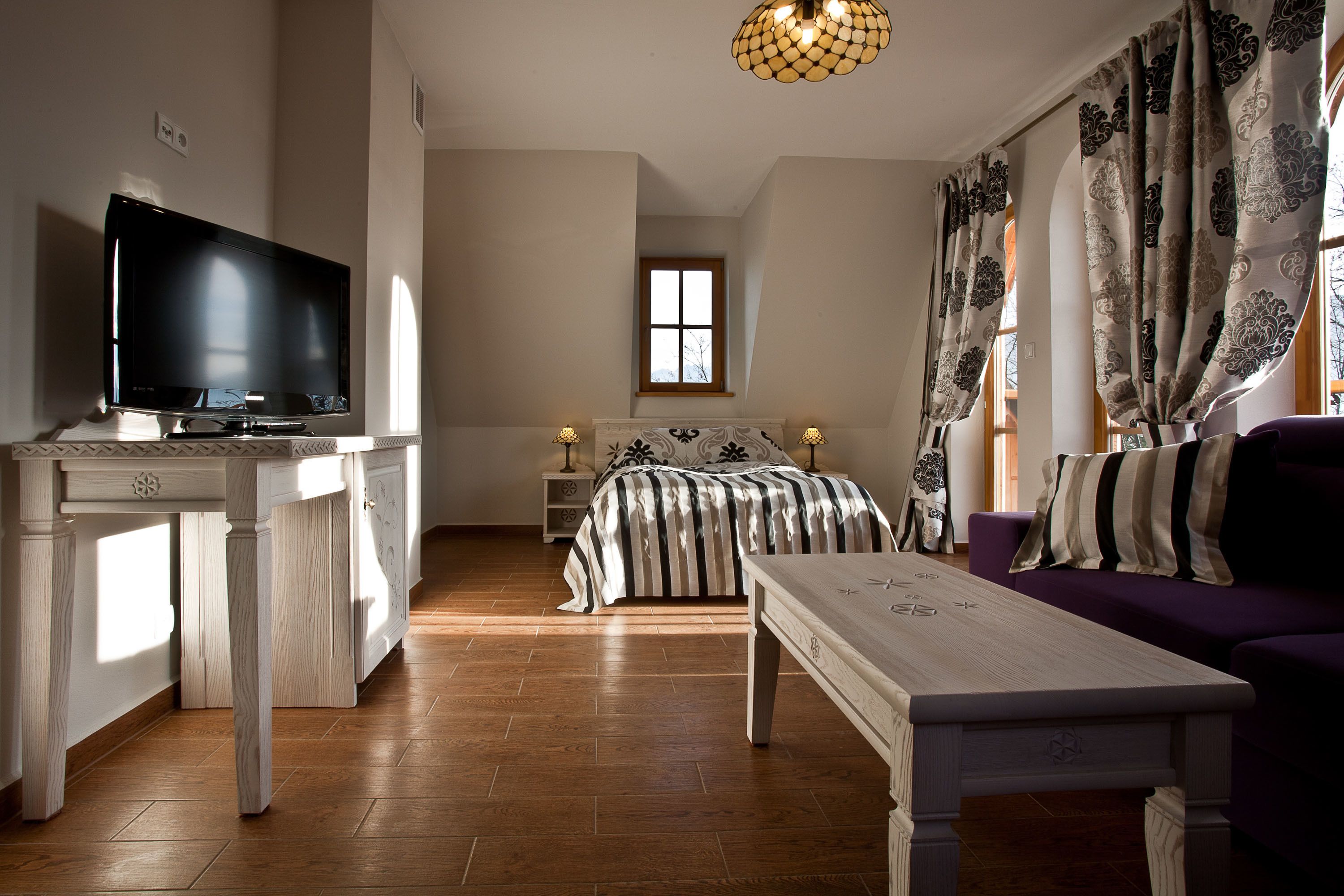A modern bedroom with a TV, a bed with striped bedding, a nightstand, and a purple sofa.