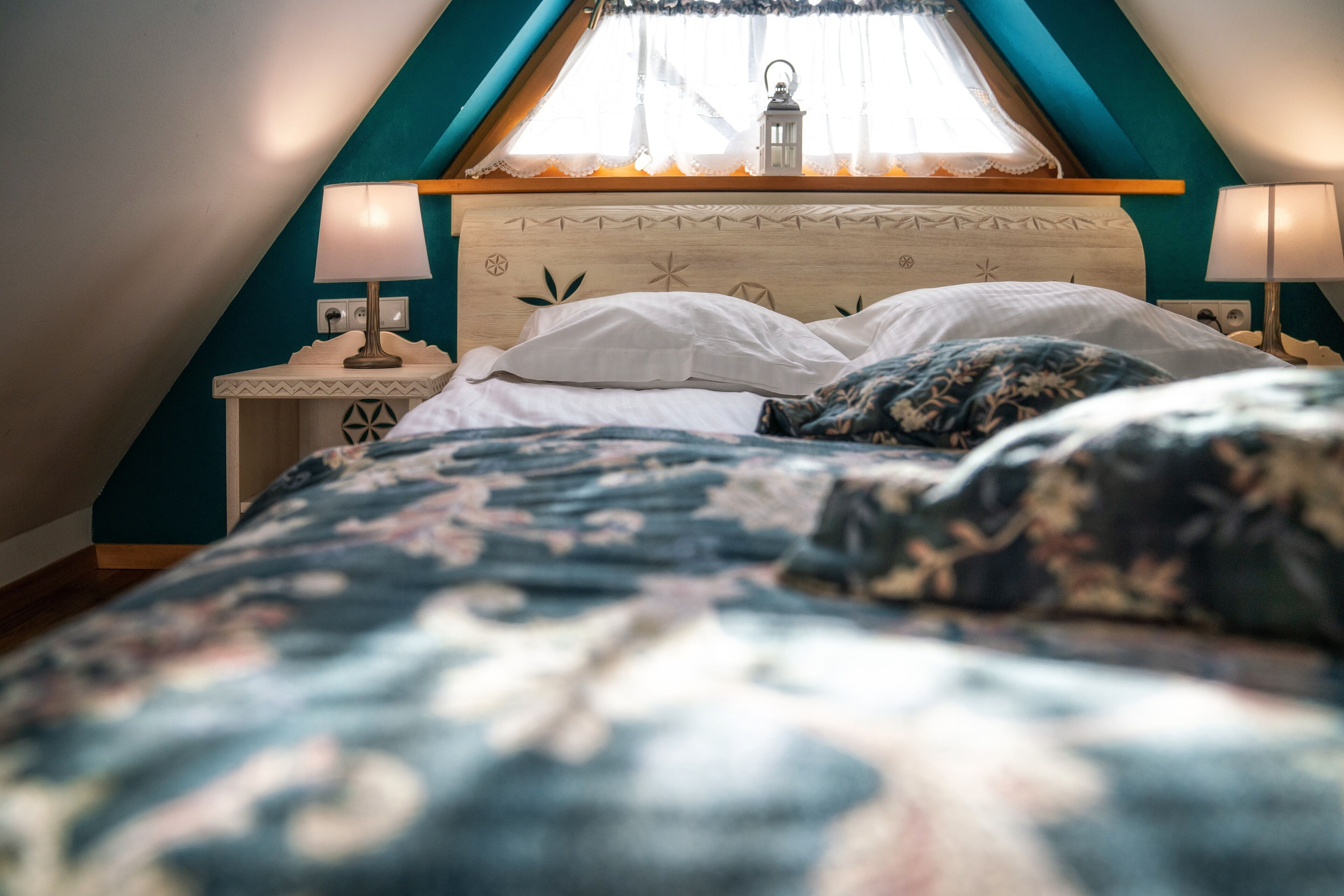 A bedroom with a sloped ceiling, a wooden headboard, two bedside lamps, and a window with a lantern.