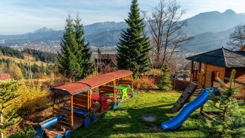 Children can play in a tranquil outdoor space surrounded by lush greenery and majestic mountains.