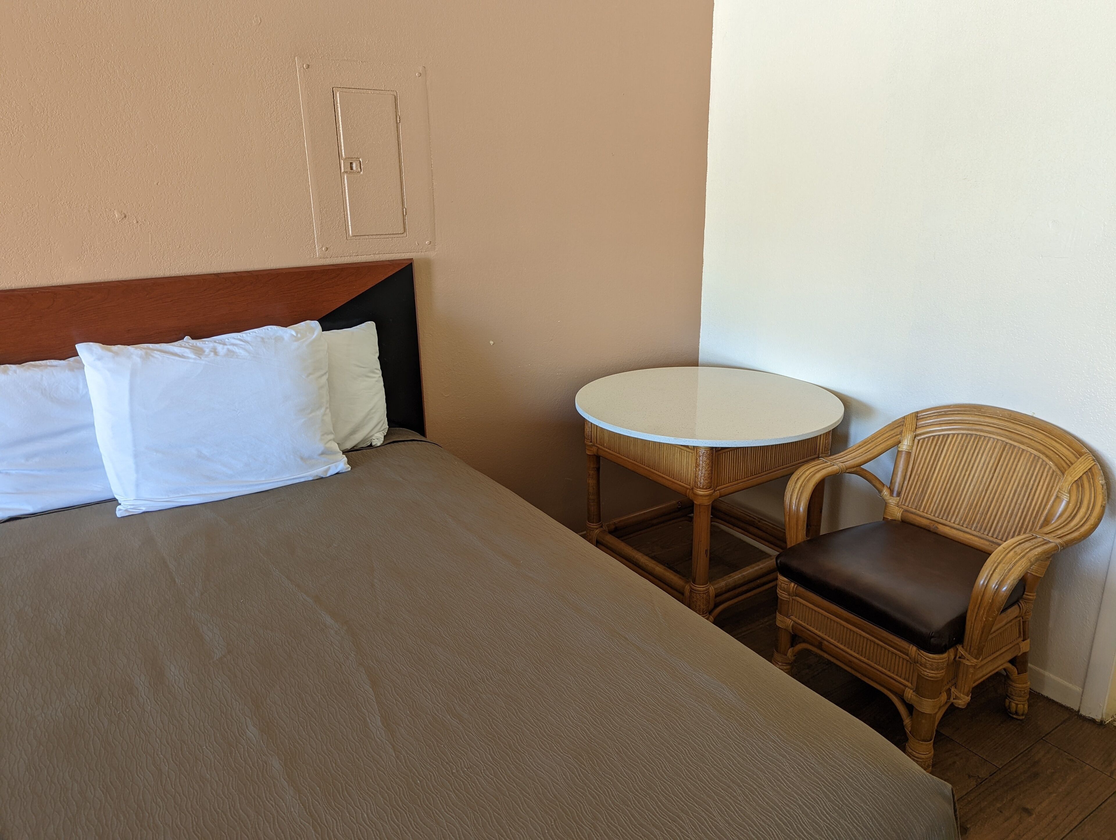 A hotel room with a bed, a small round table, and a wicker chair.