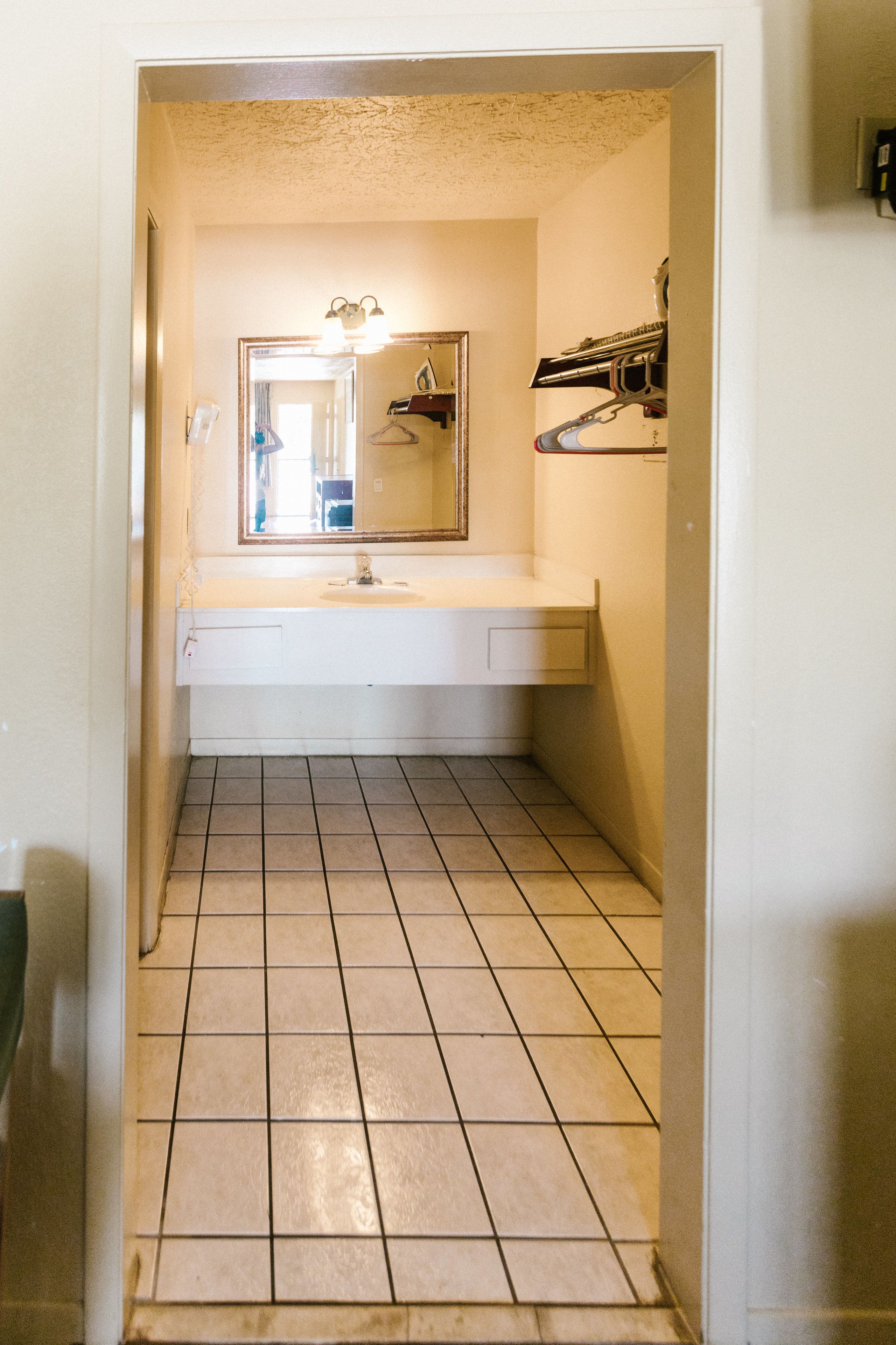 A narrow bathroom with a white sink, a mirror, and a tiled floor.