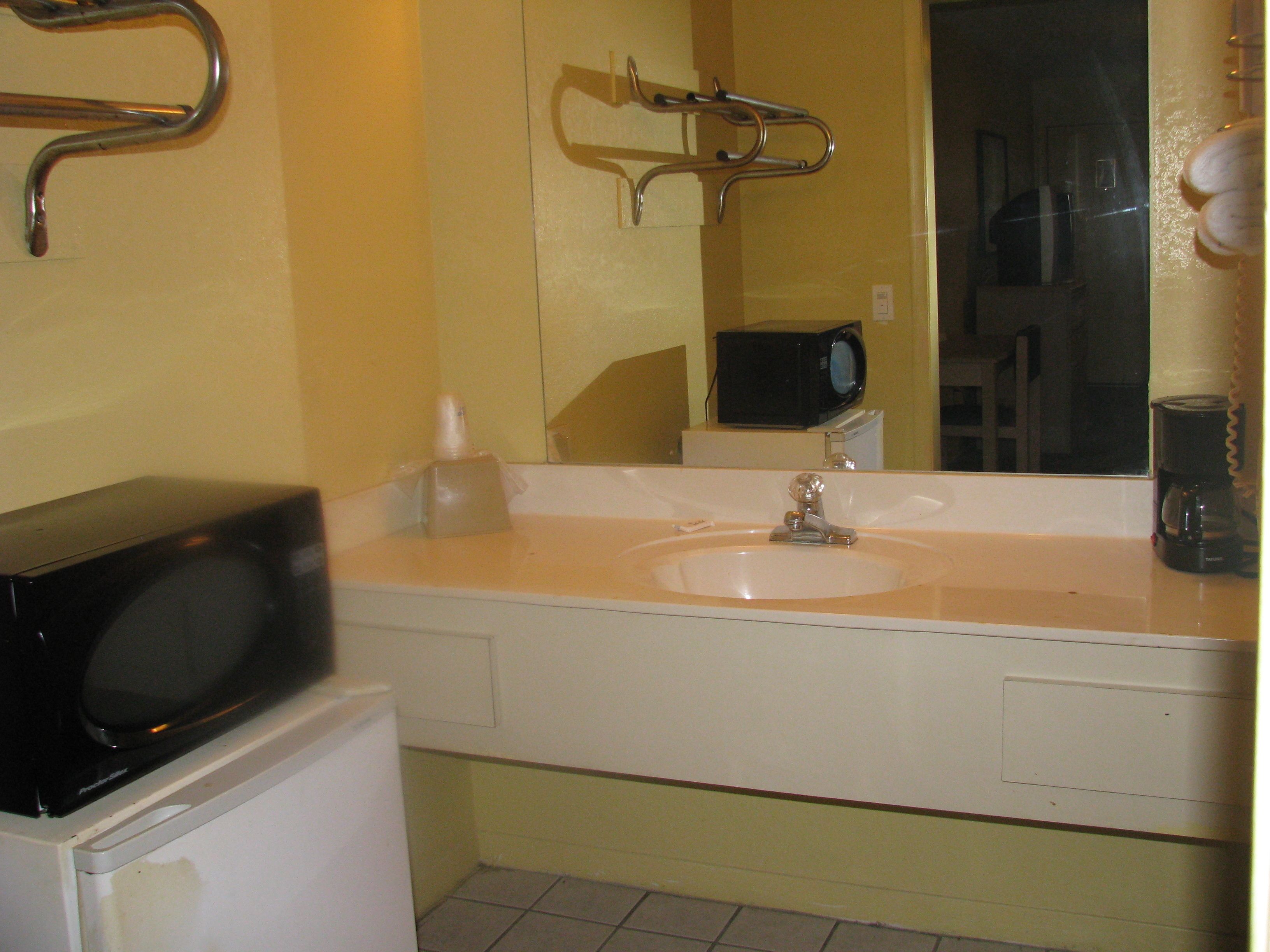 A bathroom with a sink, mirror, and a microwave on the countertop.