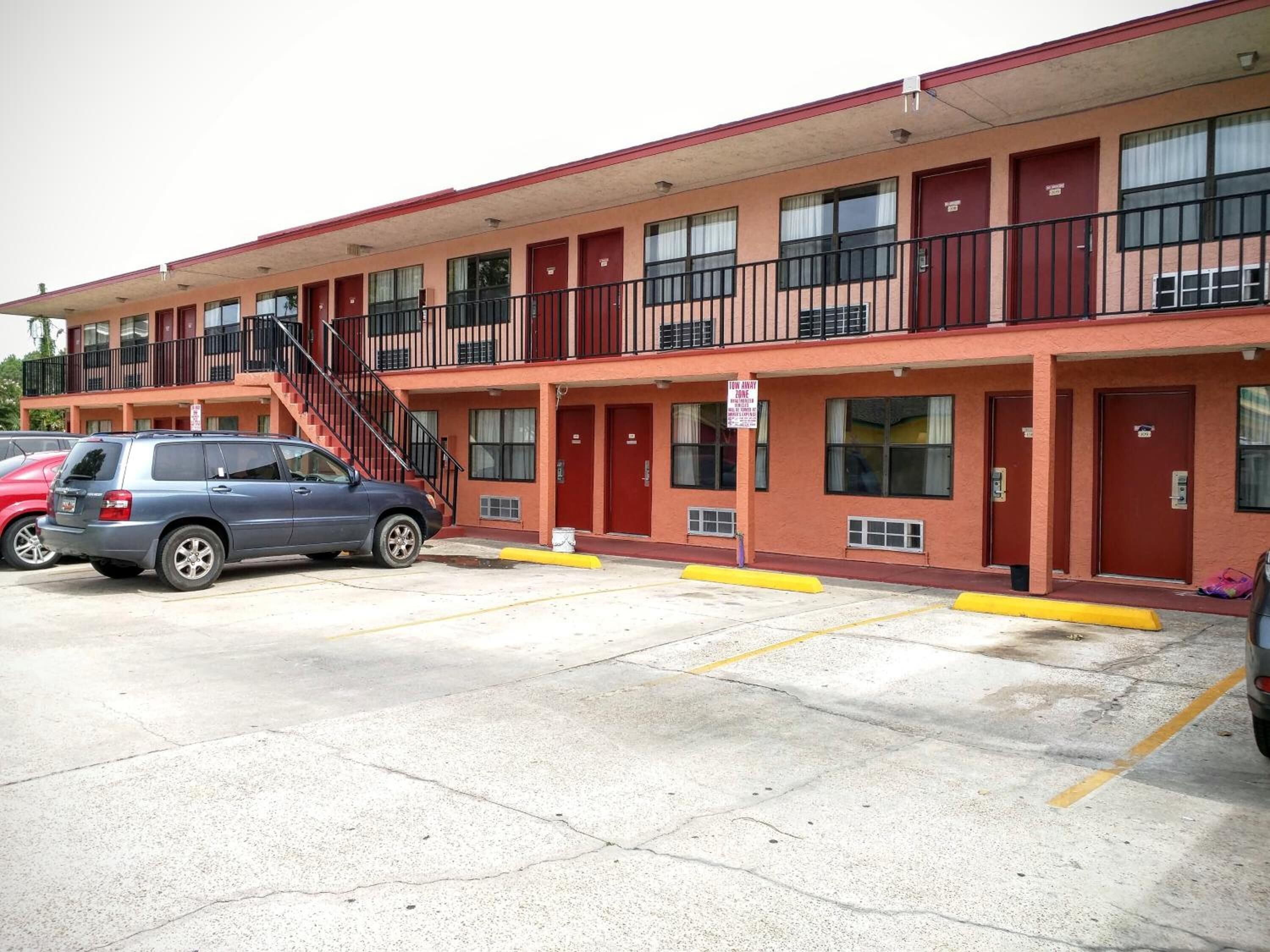 Un motel con varias habitaciones, un estacionamiento y una escalera que conduce al piso superior.