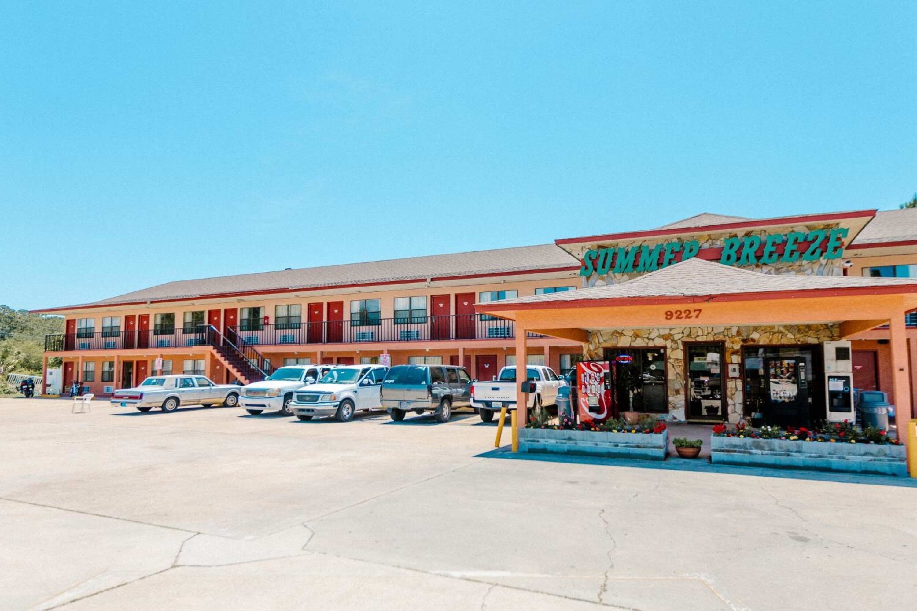 A motel with a sign reading "Summer Breeze" and the number 9227. There are several parked vehicles in front, and the building has multiple balconies.