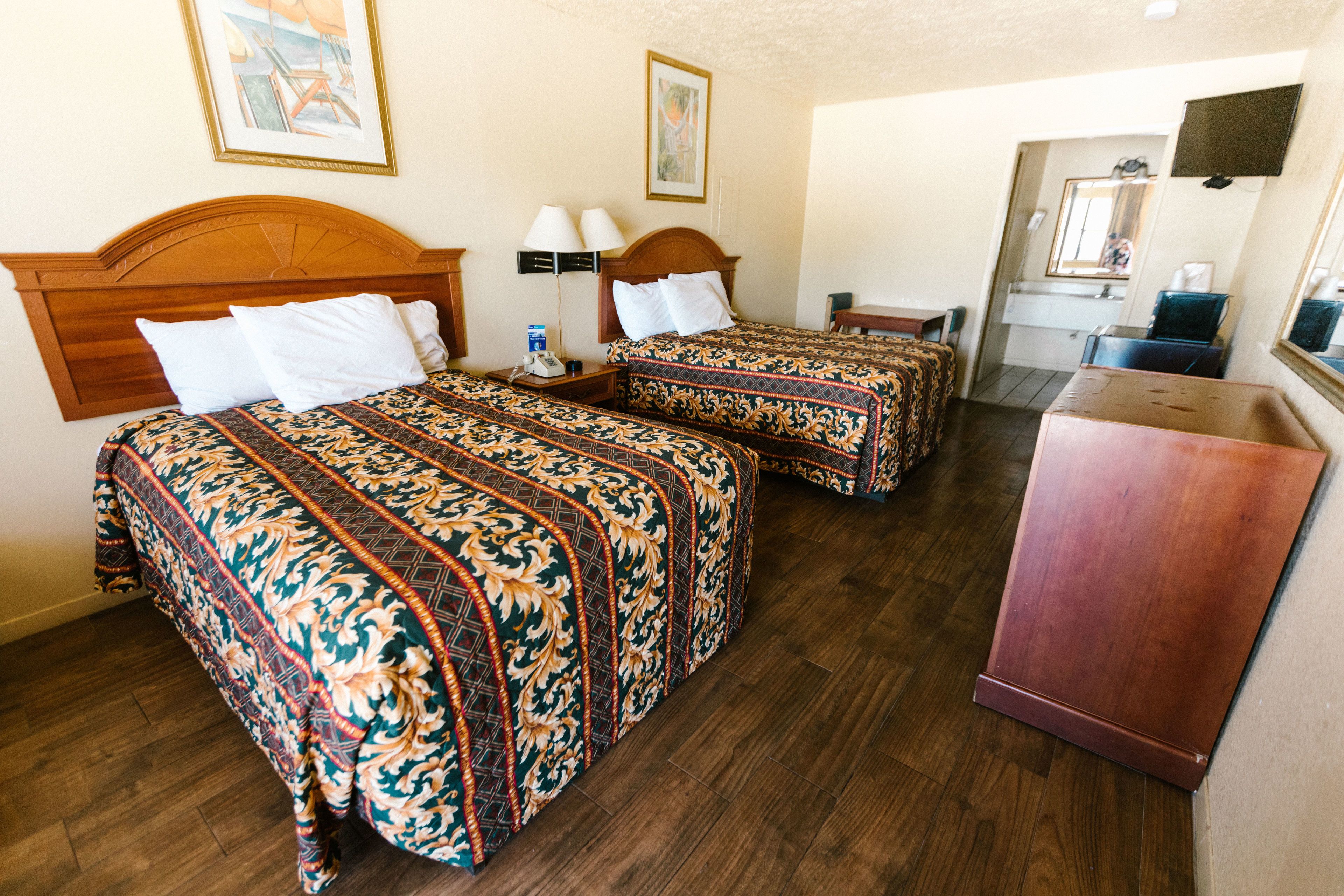 A hotel room with two beds, wooden headboards, and a desk with a mirror.
