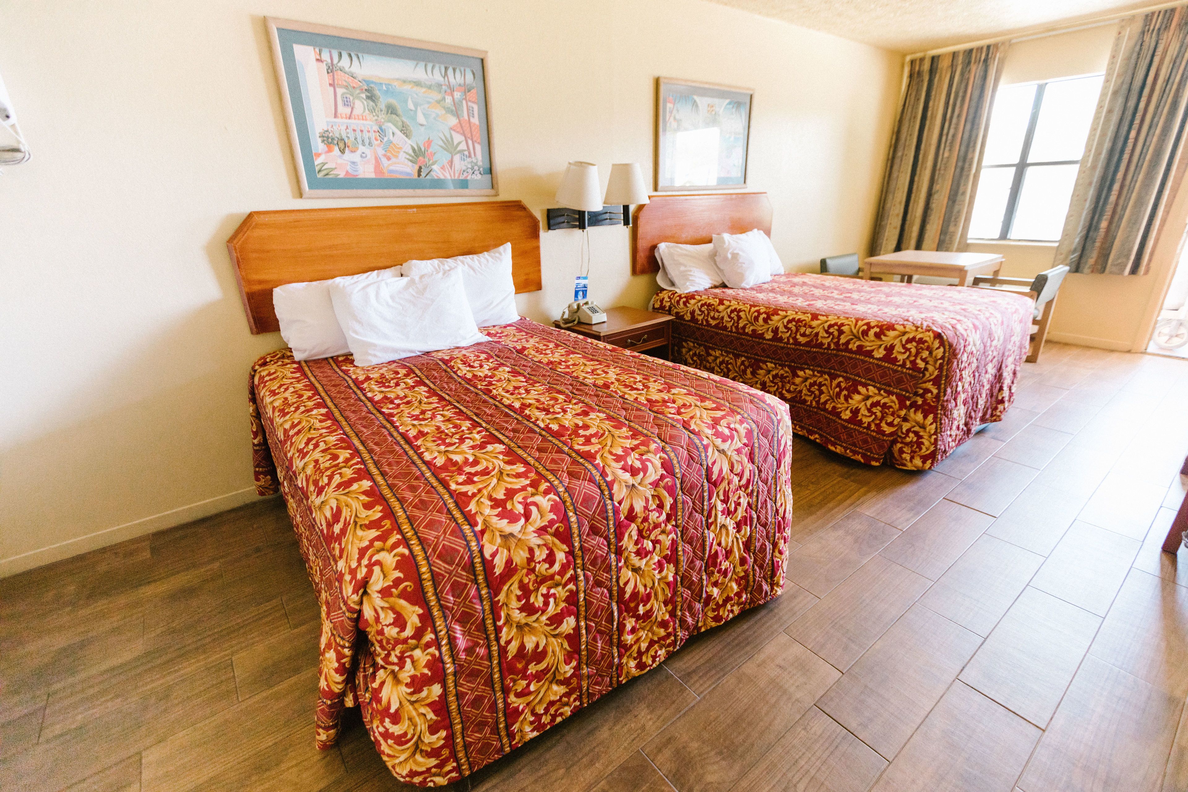 Quarto de hotel com duas camas, uma cabeceira de madeira, uma mesinha e uma cadeira.