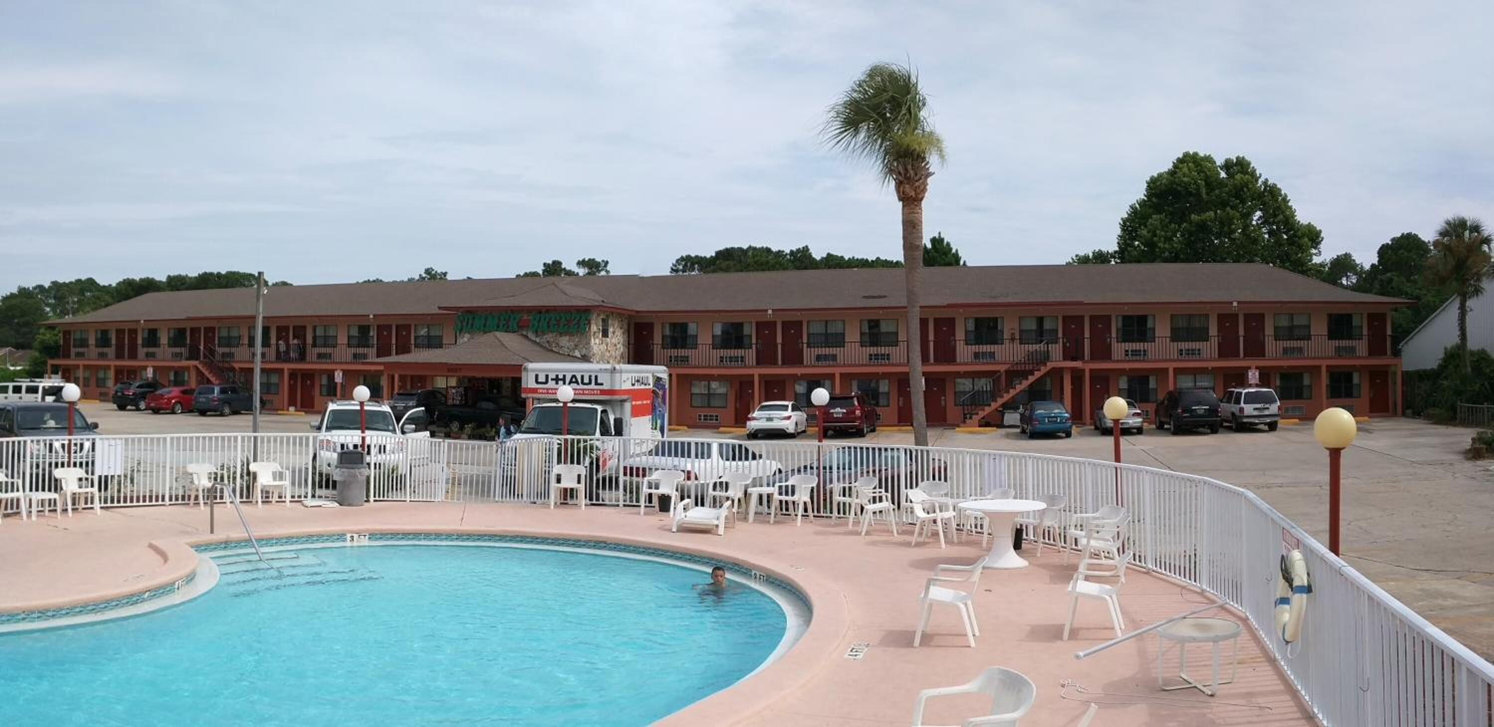 Um motel com piscina, área de estar externa e uma caminhonete U-Haul estacionada na frente.