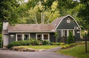 A two-story building with a dark green exterior, a pitched roof, and a front porch with a bench.
