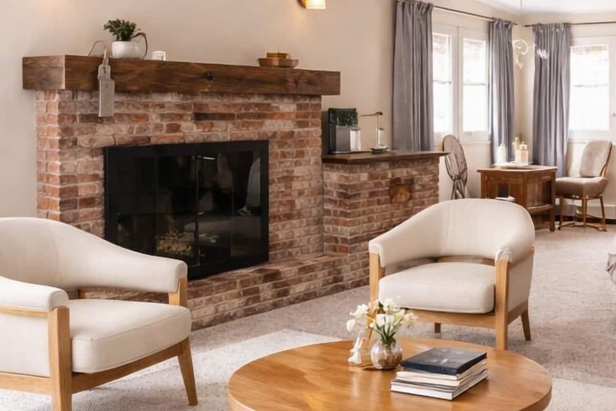 A living room with a brick fireplace, two armchairs, a round coffee table, and a television.