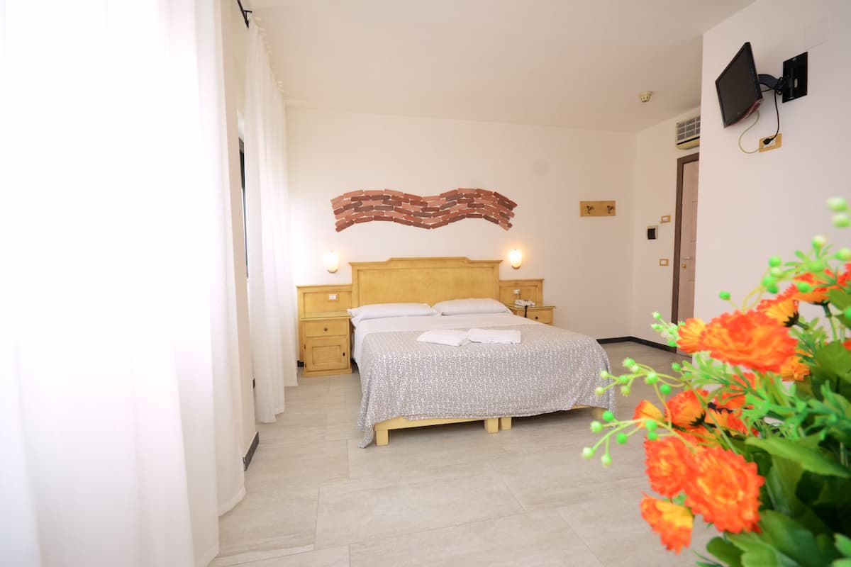 A bedroom with a wooden bed, two bedside tables, a wall-mounted TV, and a decorative brick wall piece.