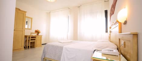 Una habitación de hotel con cama, mesita de noche, lámpara y un escritorio con silla.