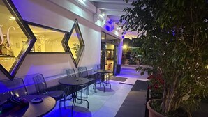 An outdoor seating area with tables and chairs, a large potted plant, and a decorative mirror on the wall. - Hotel Clinton (Casoria)