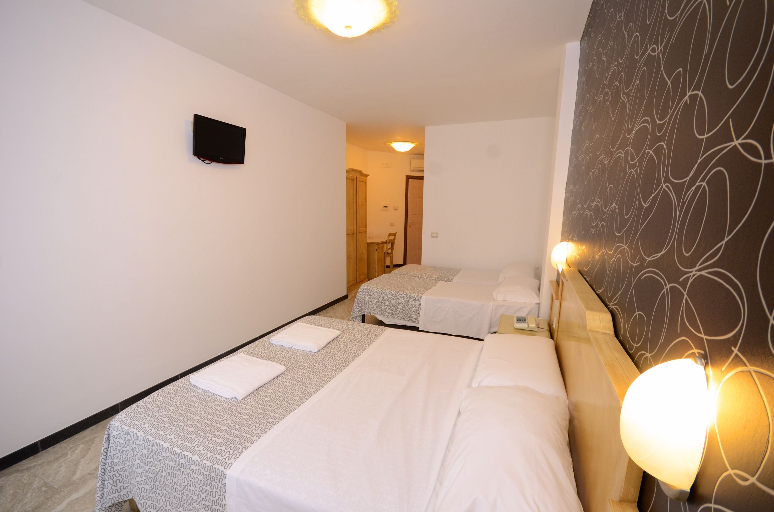 Una habitación de hotel con dos camas, un televisor de pantalla plana y una lámpara de pared.