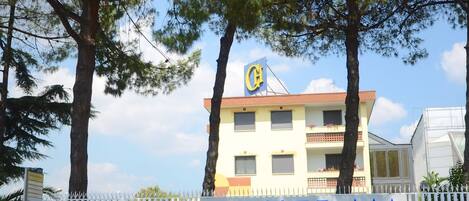 A hotel with a signboard, surrounded by a white fence, and trees in the background.