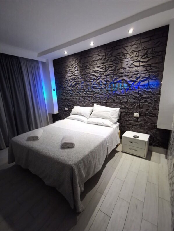 Un dormitorio moderno con un cabecero de textura de piedra, una cama bien hecha con ropa blanca y una mesita de noche con una lámpara.