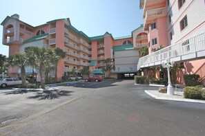 A multi-story hotel with balconies, a parking lot, and palm trees. - Beach Cottages (Indian Shores)