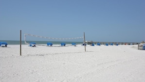 Una cancha de voleibol de playa con sillas azules y una red, rodeada de arena y un cielo despejado.