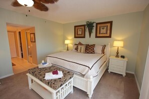 A bedroom with a bed, bedside tables, a nightstand, a small table with a chair, and a ceiling fan. - Beach Cottages (Indian Shores)