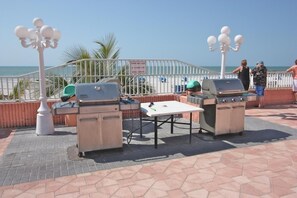 An outdoor patio with two barbecue grills, a table, and a white fence. - Beach Cottages (Indian Shores)