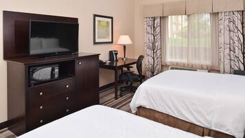 A hotel room with a TV, desk, chair, and two beds.