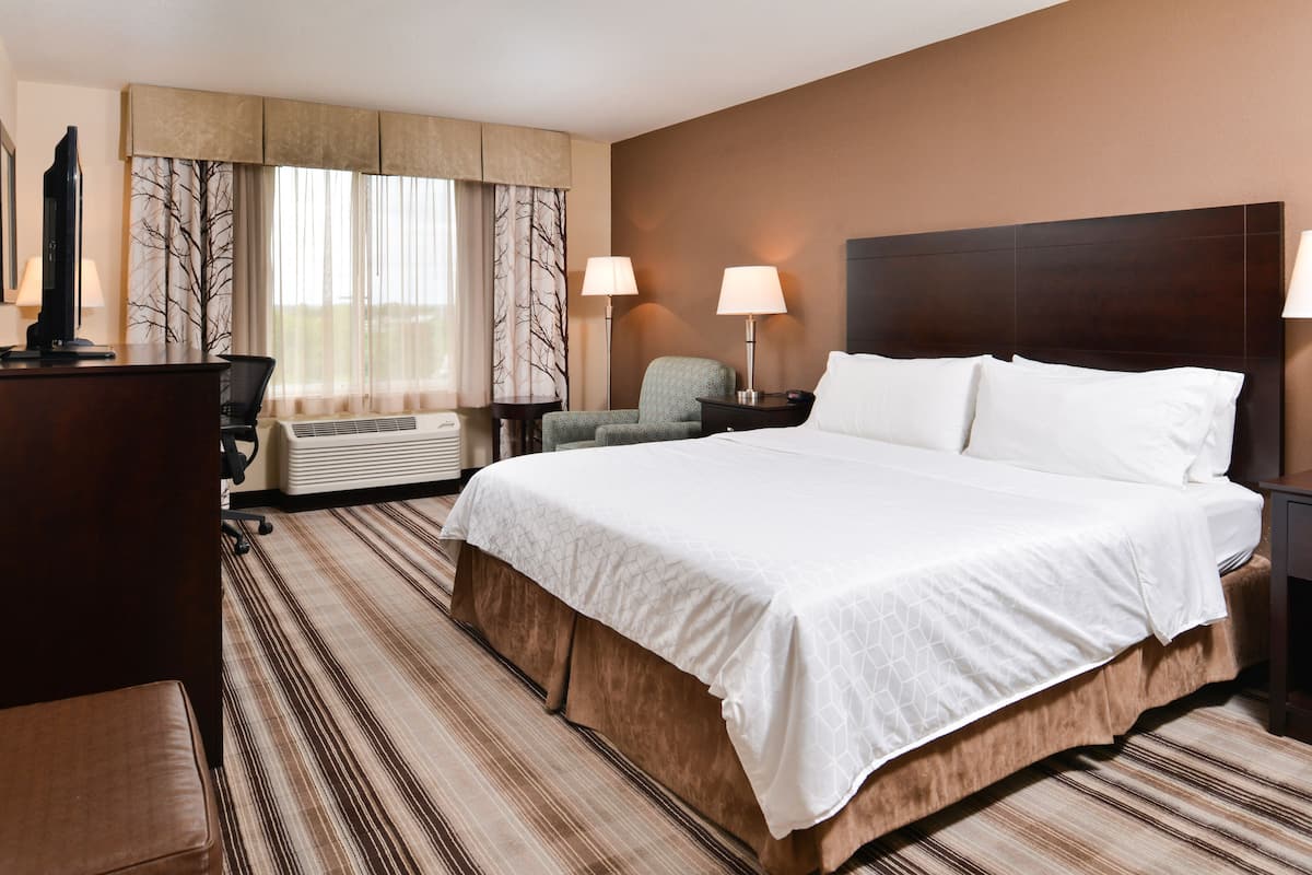 Une chambre d’hôtel avec un grand lit, deux lampes de chevet, un bureau avec un ordinateur et une chaise.
