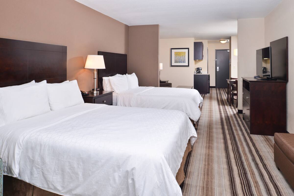 Une chambre d’hôtel avec deux lits, une télévision, un bureau et une porte donnant sur un couloir.