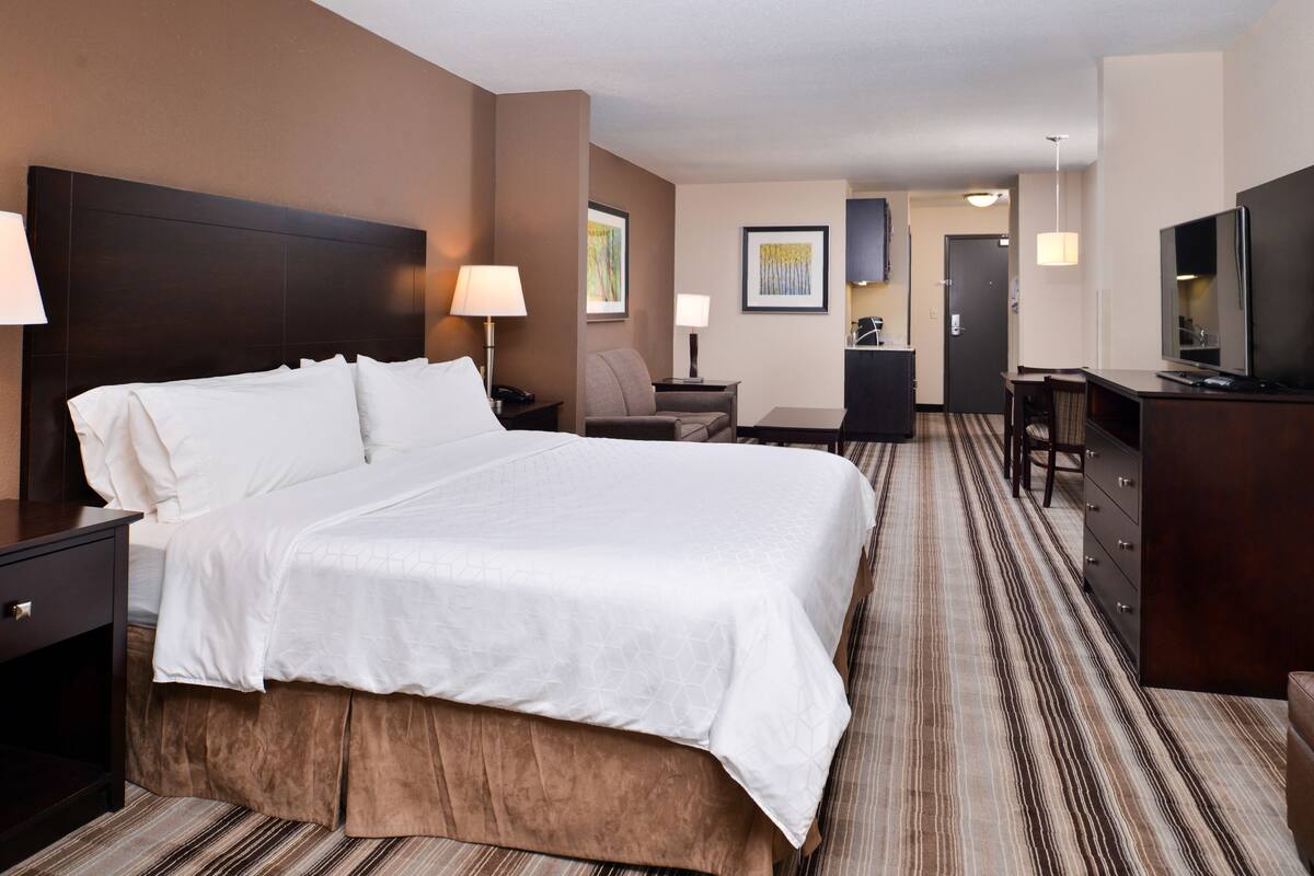 Une chambre d’hôtel avec un grand lit, un bureau, une chaise, une télévision et une commode.