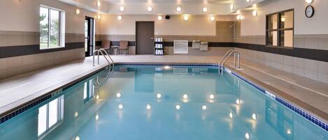 A swimming pool with a tiled deck, a door leading outside, and a clock on the wall.