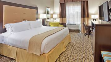 A hotel room with a large bed, a desk, a chair, a television, and a window with curtains.