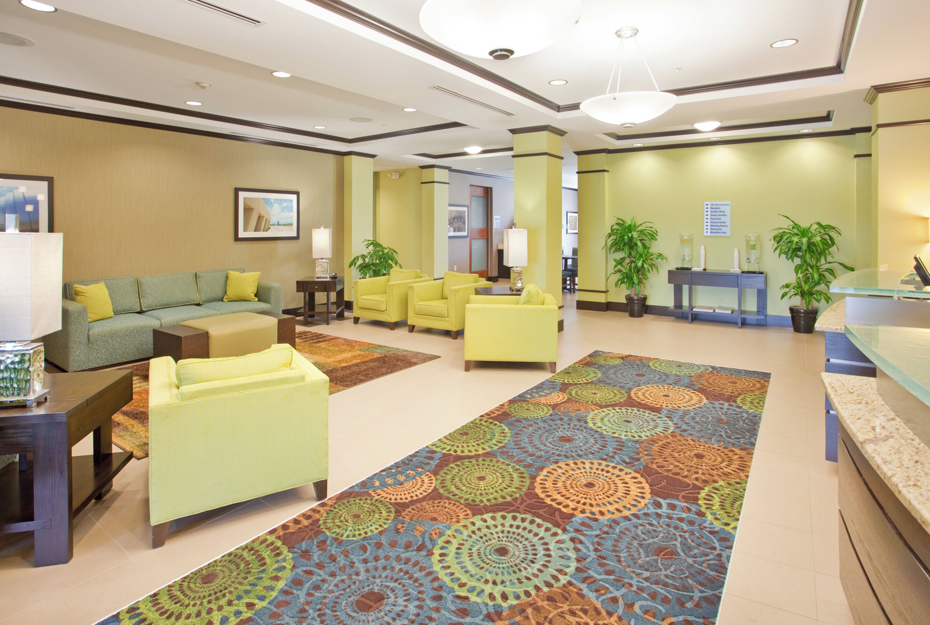 A hotel lobby with a green sofa, yellow armchairs, a patterned carpet, and a reception desk.