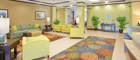 A hotel lobby with a green sofa, yellow armchairs, a patterned carpet, and a reception desk.