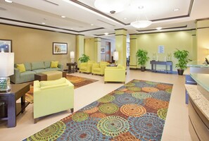 A hotel lobby with a green sofa, yellow armchairs, a patterned carpet, and a reception desk.