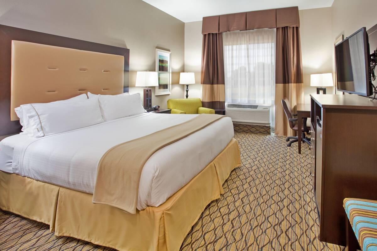 A hotel room with a large bed, a desk, a chair, a television, and a window with curtains.