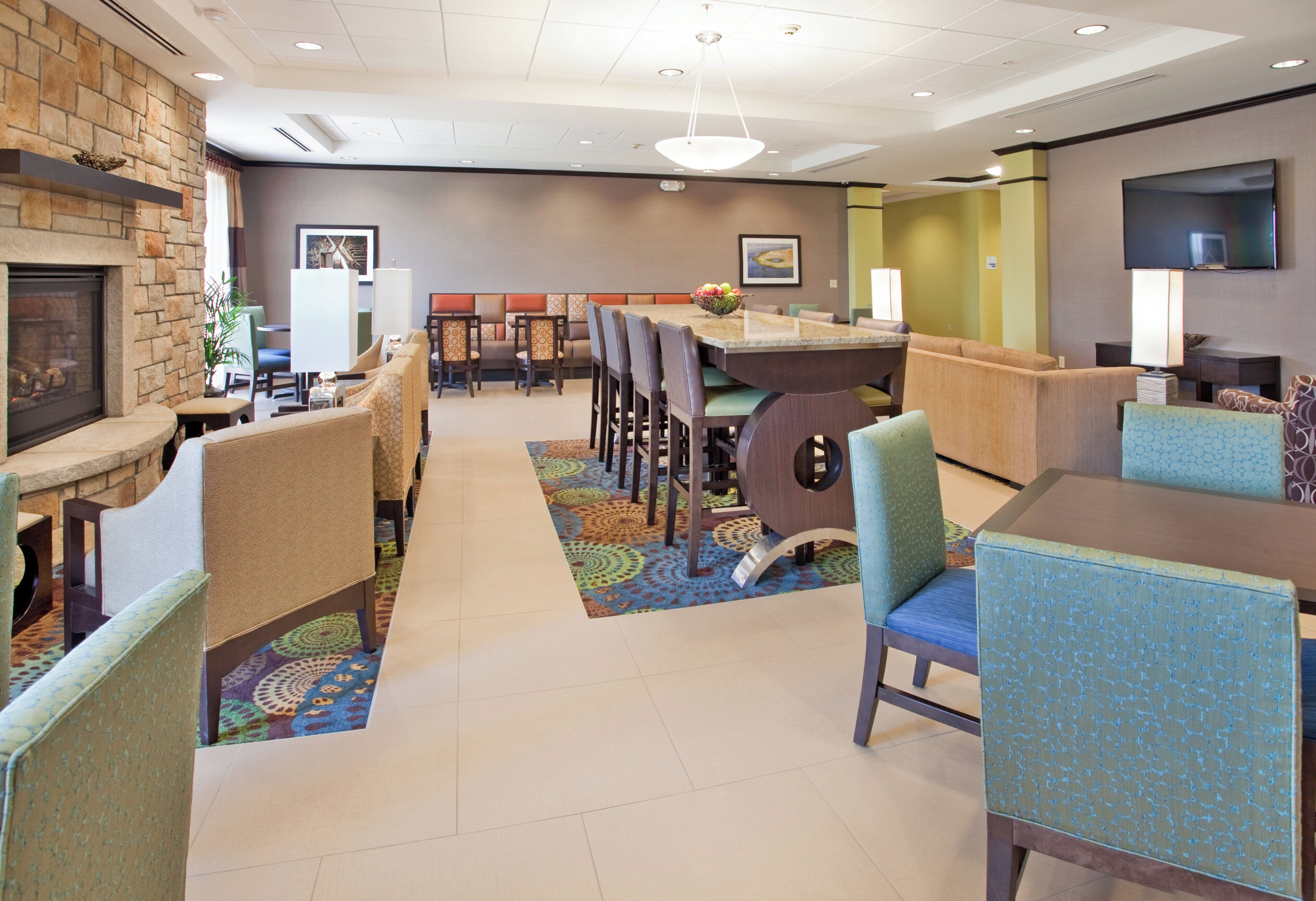 A hotel lobby with a fireplace, seating areas, a dining table, and a flat-screen TV.
