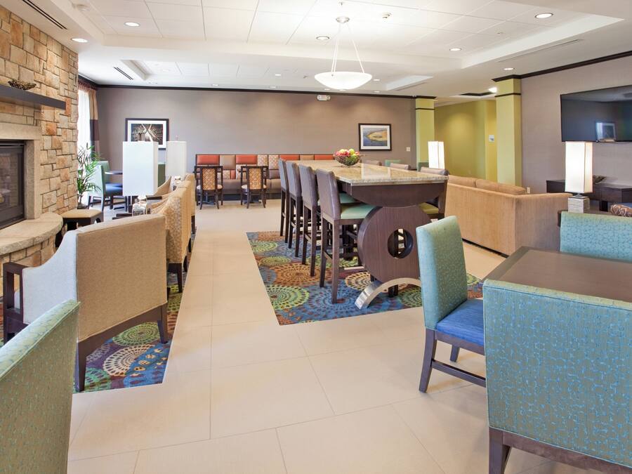 A hotel lobby with a fireplace, seating areas, a dining table, and a flat-screen TV.