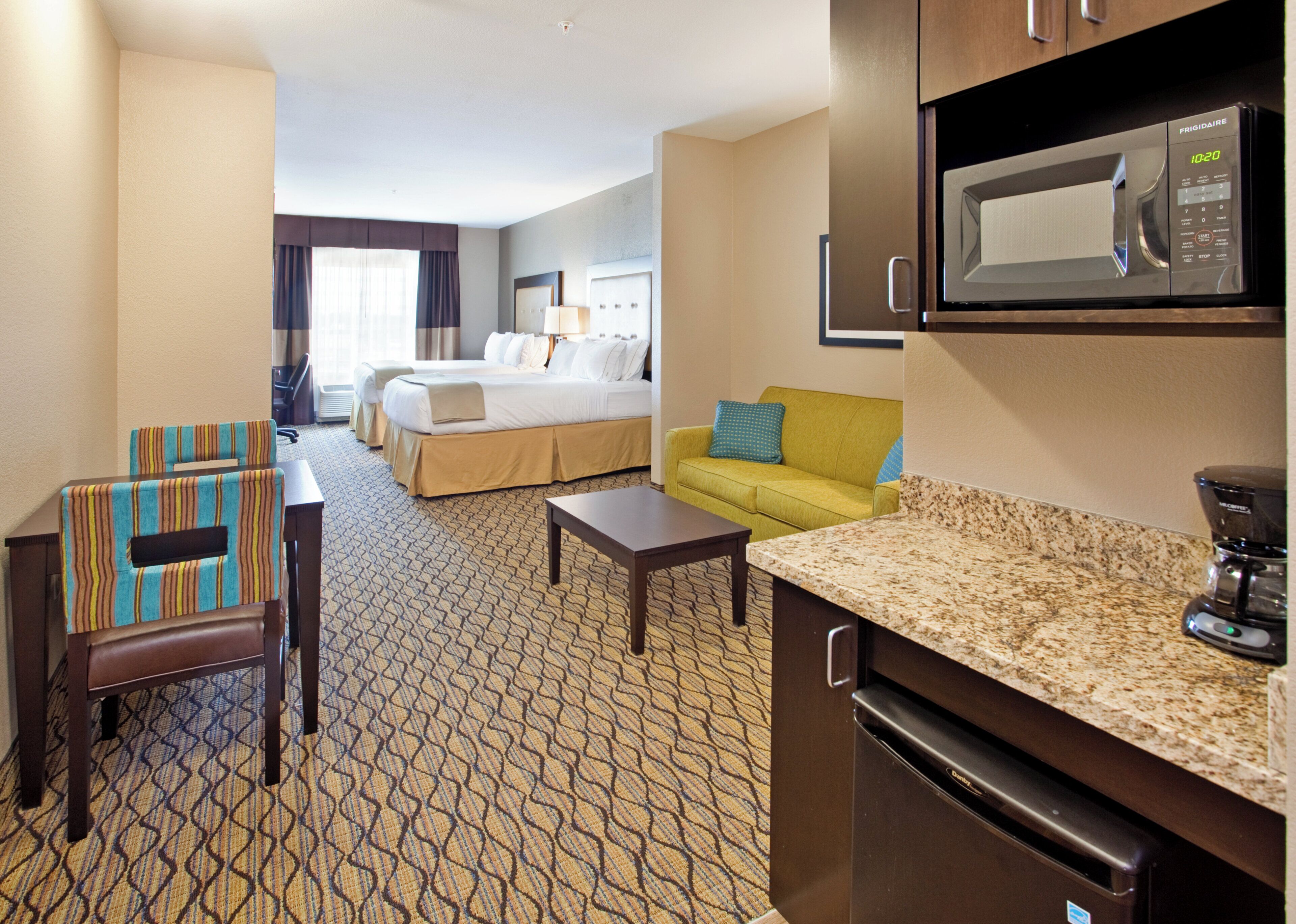 A hotel room with a bed, a sofa, a coffee table, a microwave, and a refrigerator.