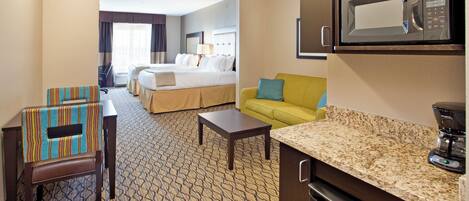 A hotel room with a bed, a sofa, a coffee table, a microwave, and a refrigerator.
