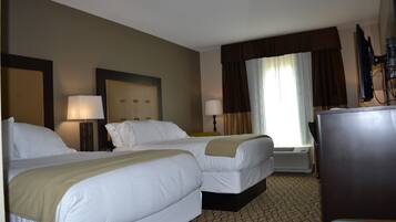 A hotel room with two beds, a desk, a television, and a window with curtains.