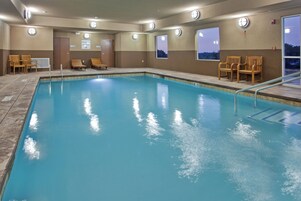 Una piscina con superficie de agua azul cristalina, rodeada de sillones de madera y una terraza con baldosas.