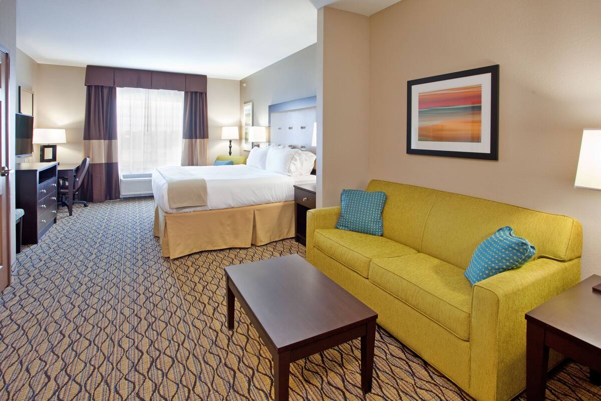A hotel room with a bed, a yellow sofa, a desk, and a chair.