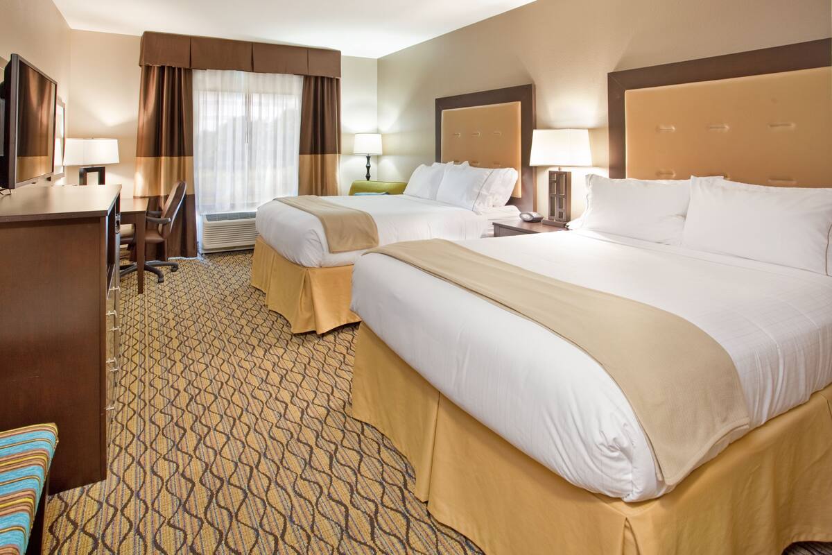 A hotel room with two beds, a desk, a chair, and a television.