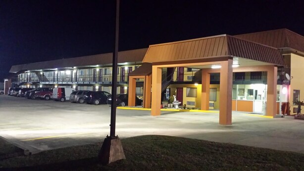 A hotel with a covered parking area, multiple floors, and a well-lit entrance. - Western Motel (Jesup)