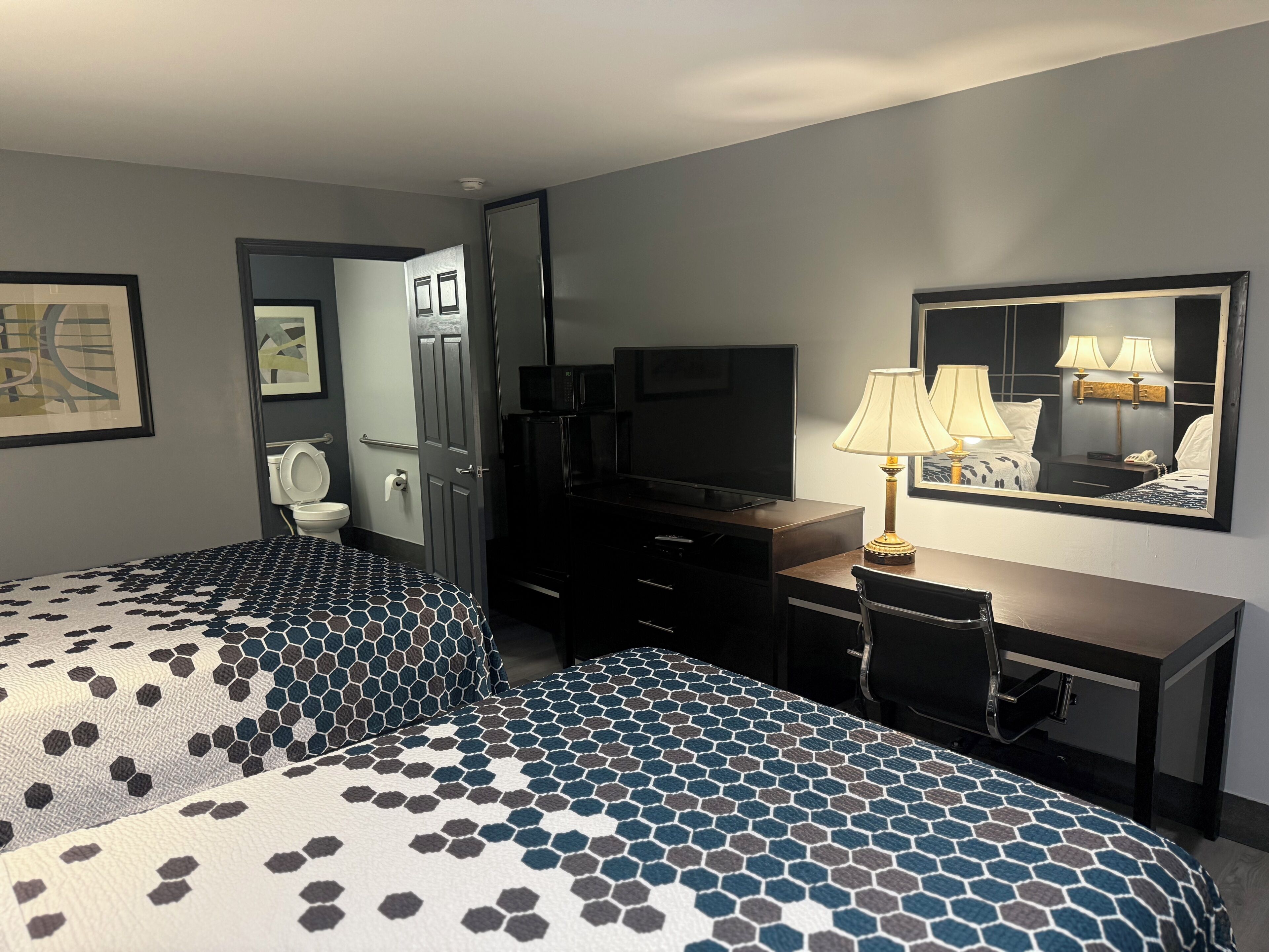 Habitación de hotel con dos camas, un escritorio, televisor, espejo y baño.