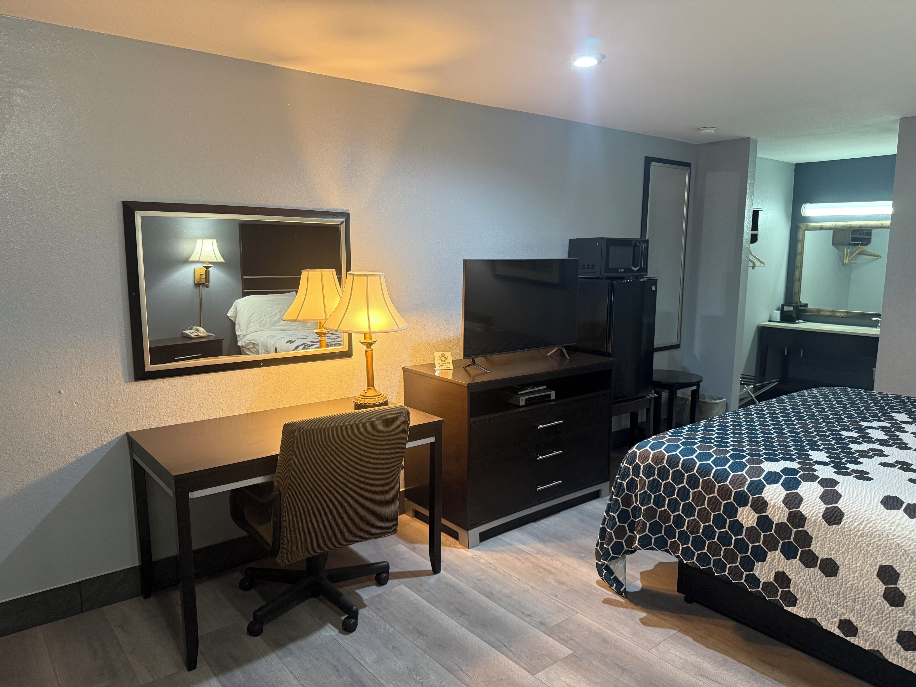 A hotel room with a desk, chair, TV, dresser, and bed.