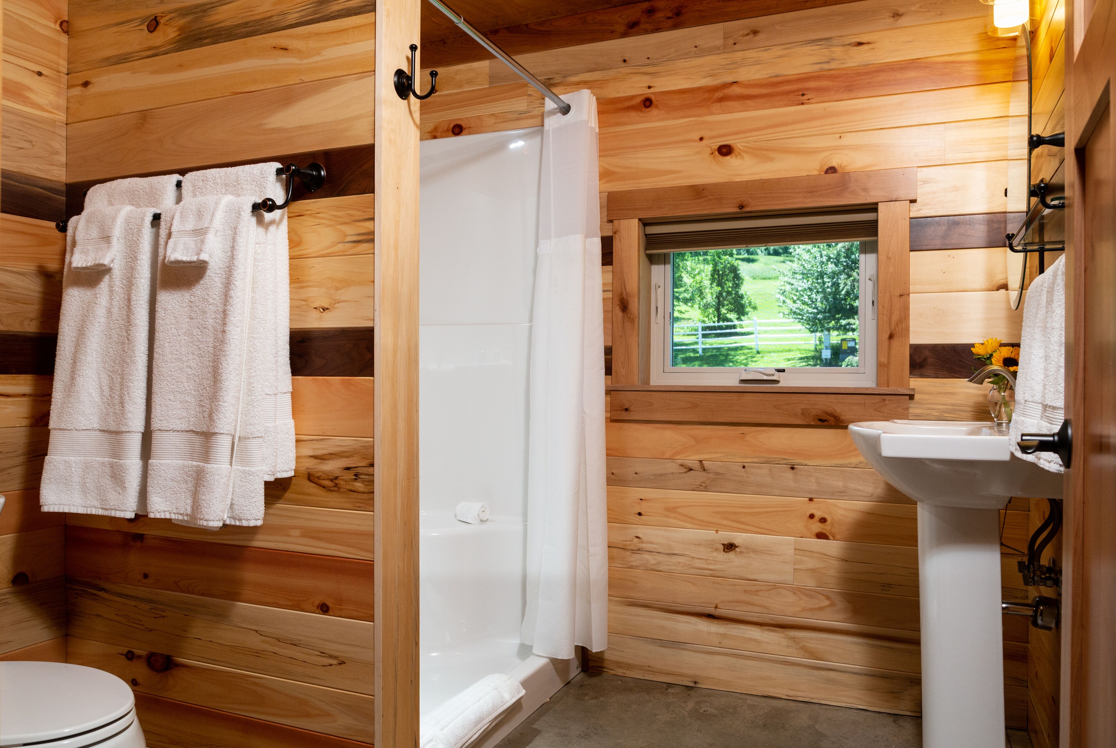 A wooden cabin bathroom with a toilet, shower, and sink.