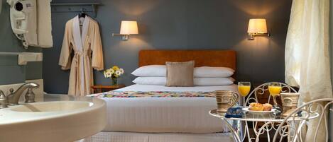 Habitación de hotel con cama, lámparas de noche, lavamanos y una mesa de desayuno con muffins y jugo.