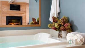 A bathroom with a bathtub, a mirror, a fireplace, and a vase with flowers. - Justin Trails Resort, LLC. (Sparta)