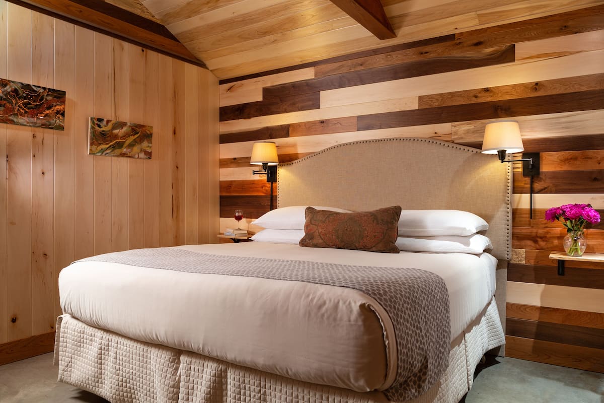 A bedroom with a large bed, two bedside lamps, a nightstand with a wine glass, and a vase with flowers.