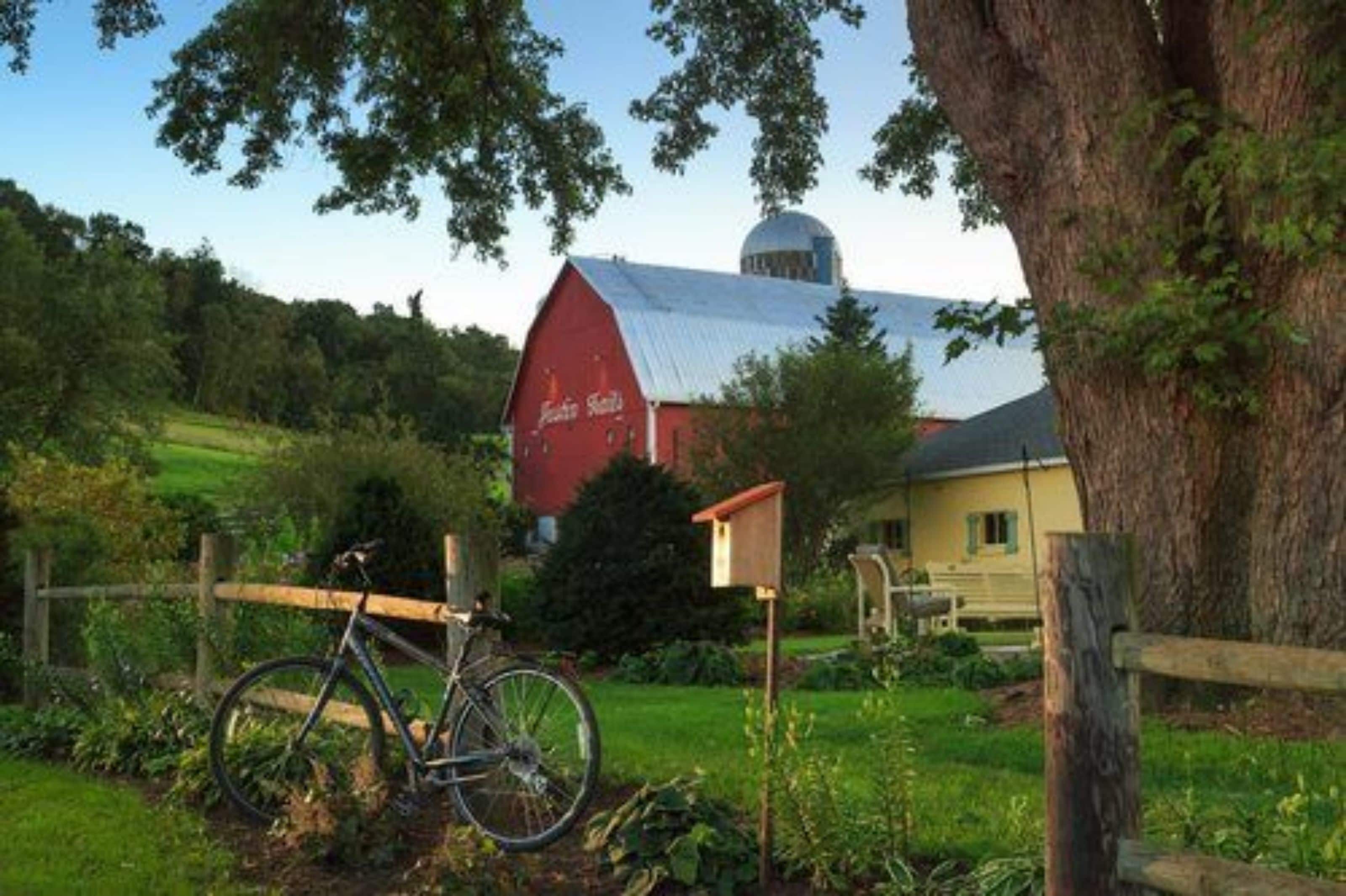 A red barn with a blue roof, a bicycle, and a small wooden structure in a rural setting.