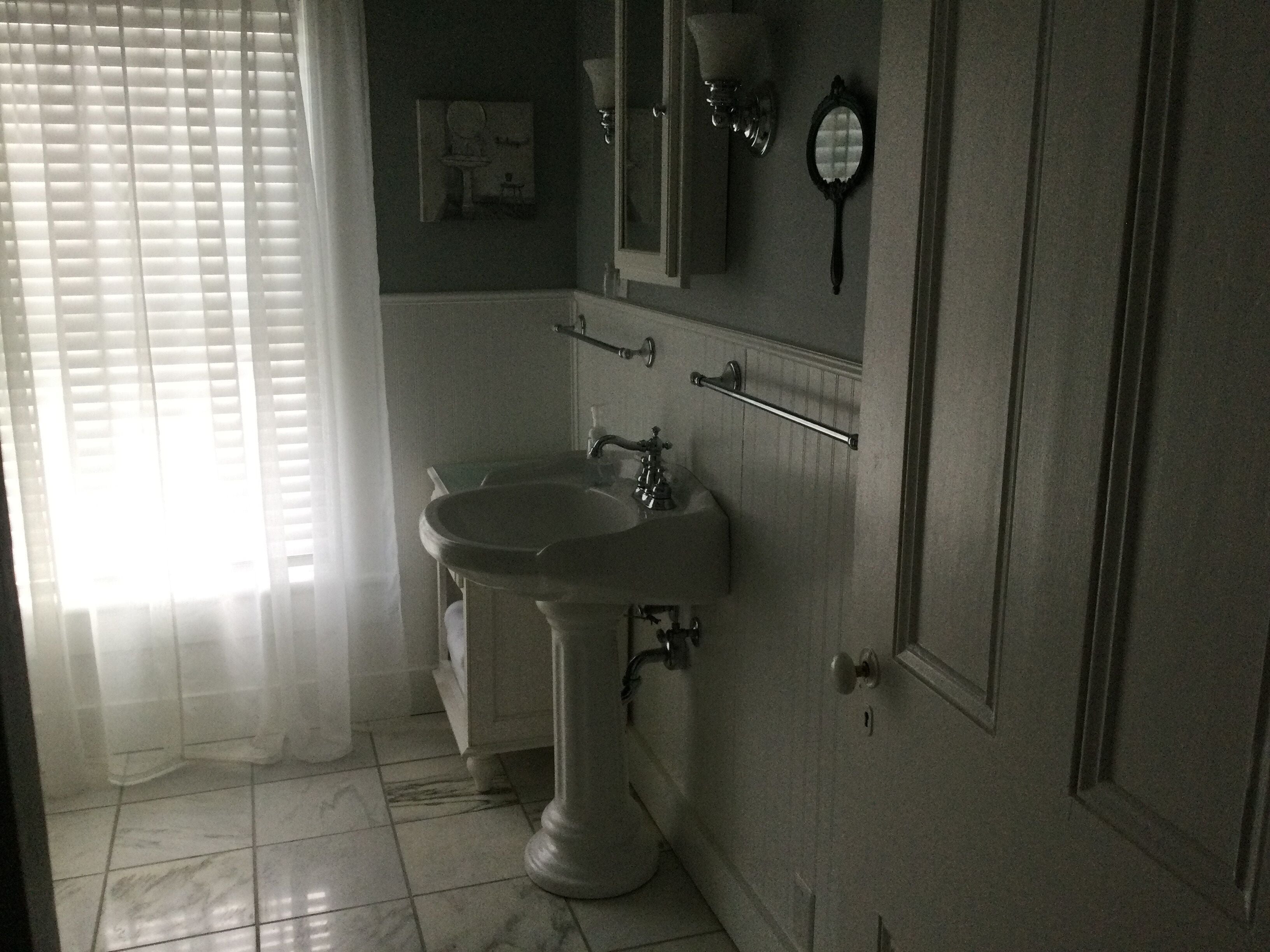 Une salle de bain avec un lavabo sur colonne, un miroir, un porte-serviettes et une porte.